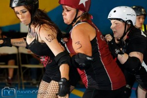 V Town Darlings Sarah Gasca and Christina Chandler lock in their opponent during a recent game with the Pacific Coast Recycled Rollers. Photo by David Costa.